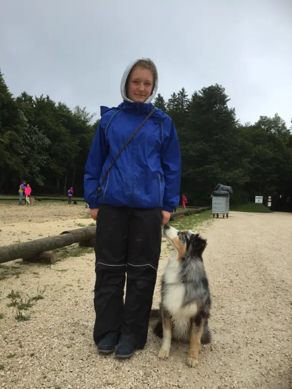 Eine Frau in einer blauen Jacke und schwarzer Hose neben einem Hund stehend. – Jugend und Hund Lager 2017 in Balmberg