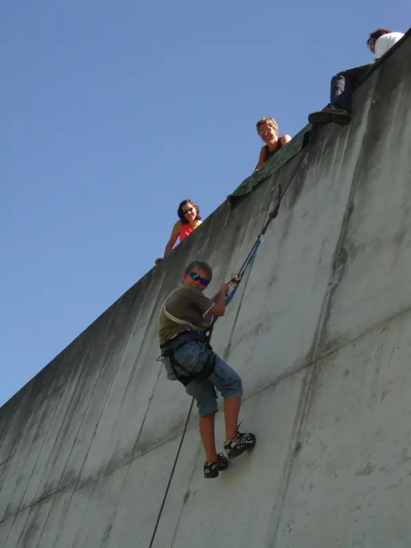 Eine Gruppe von Menschen, die die Seite einer Betonwand hinaufklettern, wobei eine Person im Vordergrund ein Seil hält. – Jugend und Hund Lager 2010 in Brigels
