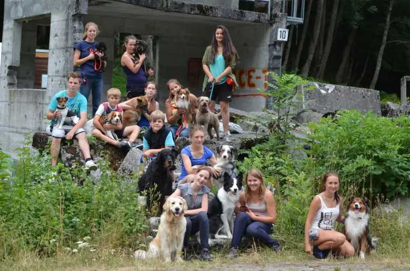 Eine Gruppe von Menschen, die auf einem Hügel mit Hunden sitzen. – Jugend und Hund Lager 2013 in Chur