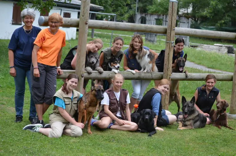 Eine Gruppe von Menschen und Hunden, die auf dem Gras sitzen. – Jugend und Hund Lager 2013 in Chur