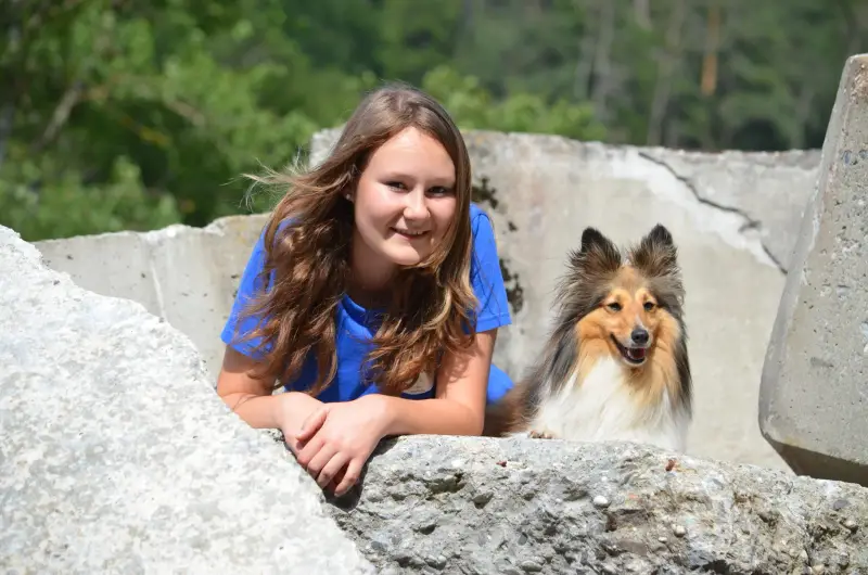 Ein Mädchen sitzt auf einem Felsen mit einem Hund. – Jugend und Hund Lager 2014 in Chur
