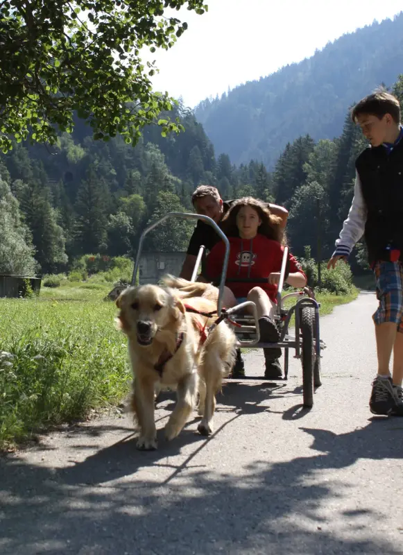 Eine Frau, die ein Kind im Rollstuhl schiebt. – Jugend und Hund Lager 2014 in Chur