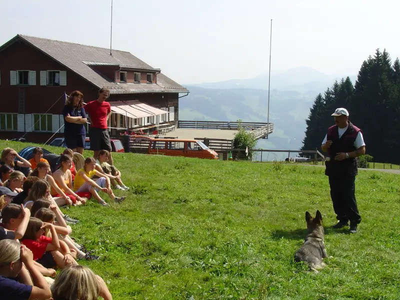 Eine Gruppe von Menschen, die auf einem Hügel sitzen. – Jugend und Hund Lager 2005 in Ebnatkappel
