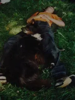 Das Bild zeigt einen Mann, der mit seinem Hund im Gras liegt, trägt ein orangefarbenes T-Shirt und blaue Jeans. – Jugend und Hund Lager 2001 in Eigenthal