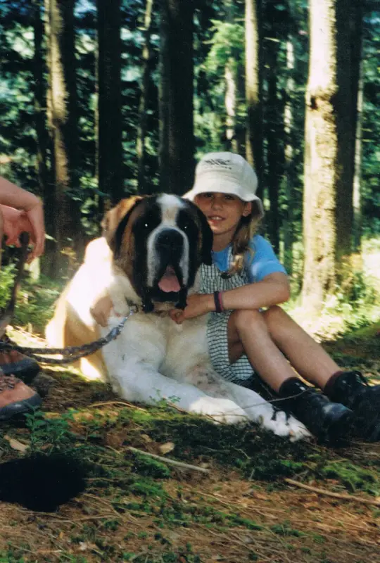 Ein junges Mädchen, das auf dem Boden neben einem grossen Hund sitzt und ein blau-weisses Kleid und eine weisse… Rasse: Bernhardiner. – Jugend und Hund Lager 2001 in Eigenthal