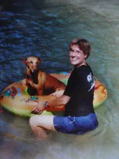 Das Bild zeigt einen Mann im Wasser mit einem Hund auf einem aufblasbaren Ring, beide lächelnd. – Jugend und Hund Lager 2001 in Eigenthal