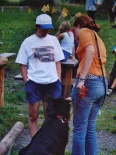 Das Bild zeigt einen Mann und eine Frau, die neben einem schwarzen Hund an der Leine stehen. Rasse: Belgischer Schäferhund (Groenendael). – Jugend und Hund Lager 2001 in Eigenthal