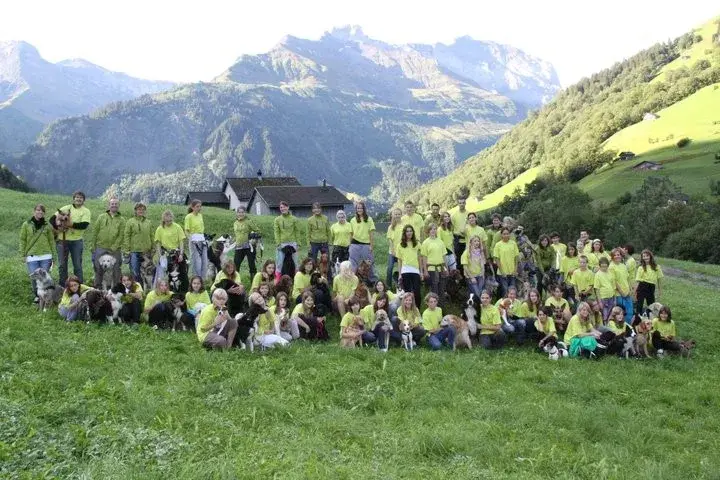 Eine Gruppe von Menschen in grünen Hemden posiert für ein Foto auf einem Grasfeld mit ihren Hunden. – Jugend und Hund Lager 2011 in Elm