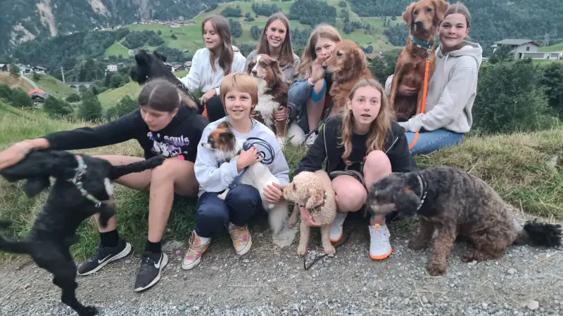 Eine Gruppe von Menschen, die auf einem Hügel sitzen, lächelnd… Rassen: Lakeland Terrier, Curly-Coated Retriever, Zwergpudel, Irish Setter. – Jugend und Hund Lager 2023 in Segnas