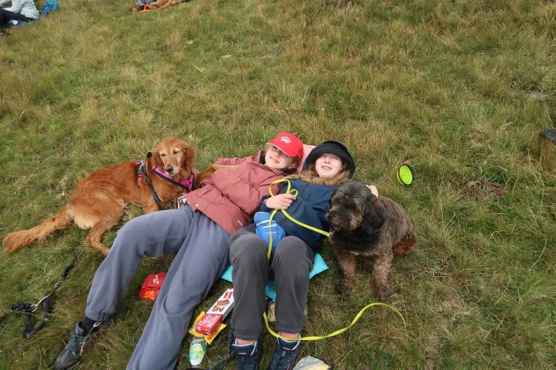 Zwei Personen, die mit ihren Hunden auf einer Decke sitzen. Rasse: Golden Retriever. – Jugend und Hund Lager 2023 in Segnas