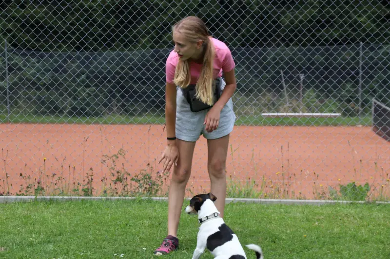 Eine Frau, die auf einem üppigen grünen Feld neben einem kleinen Hund steht. Rasse: American Staffordshire Terrier. – Jugend und Hund Lager 2025 in Segnas
