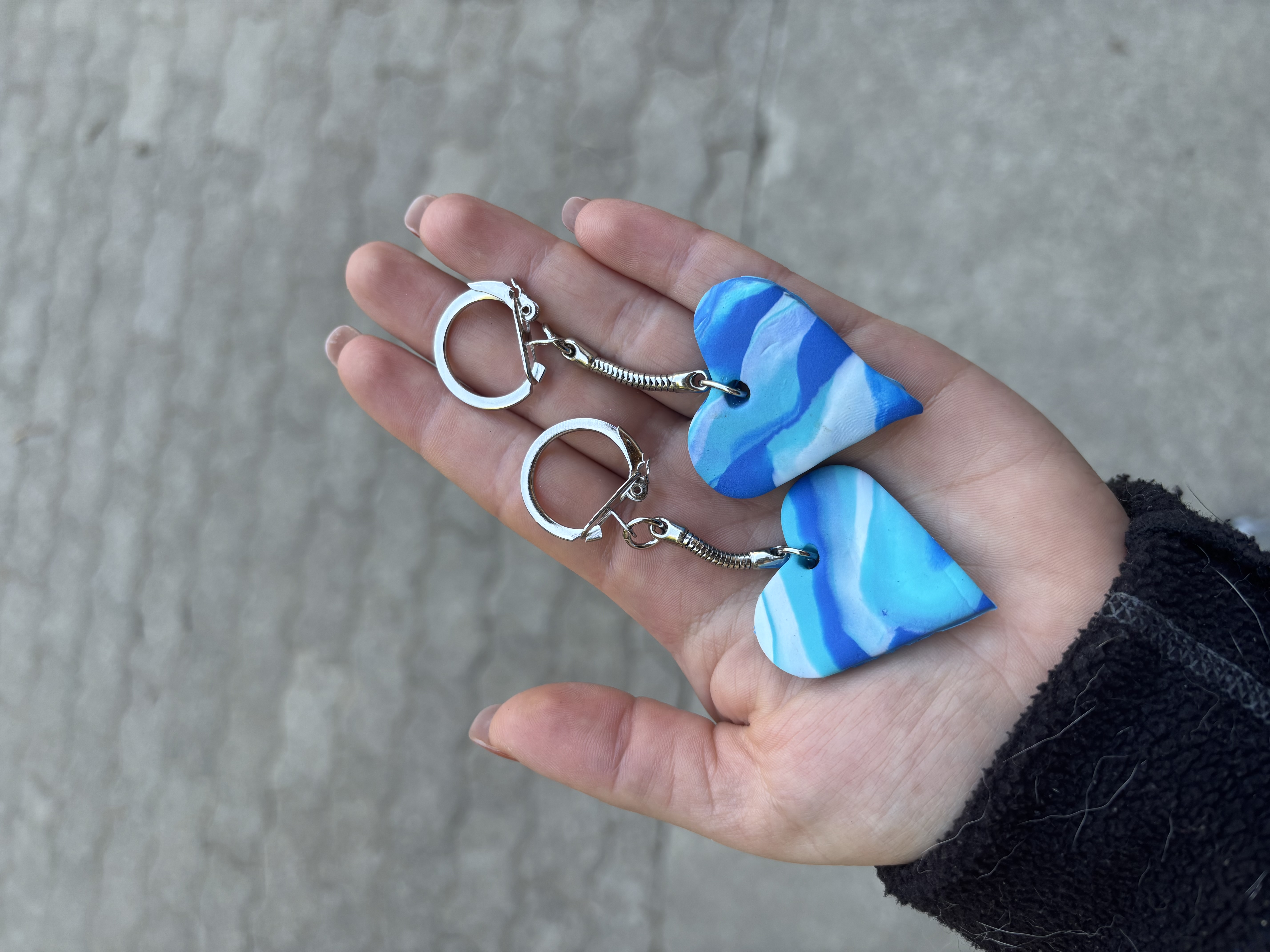 Das Bild zeigt eine Person, die ein Paar blau-weiß marmorierte Ohrringe in der Hand hält, mit einer Wand im Hintergrund. Die Ohrringe haben ein einzigartiges Muster aus abwechselnd blau und weiß, und die Hand der Person ist sichtbar, zeigt die komplizierten Details der Ohrringe. Aktivität: Wandern (hiking).