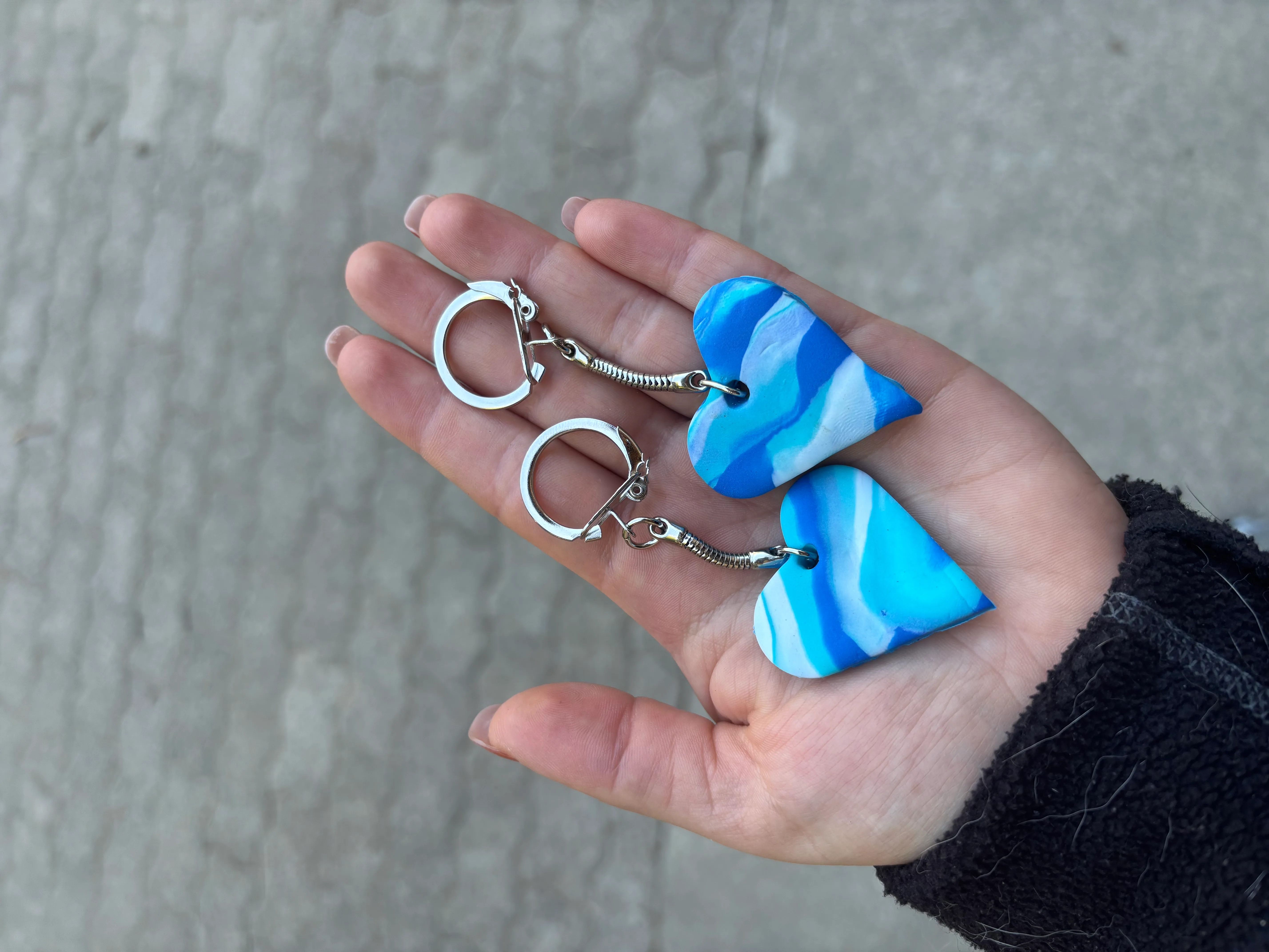 Das Bild zeigt eine Person, die ein Paar blau-weiß marmorierte Ohrringe in der Hand hält, mit einer Wand im Hintergrund. Die Ohrringe haben ein einzigartiges Muster aus abwechselnd blau und weiß, und die Hand der Person ist sichtbar, zeigt die komplizierten Details der Ohrringe. Aktivität: Wandern (hiking).