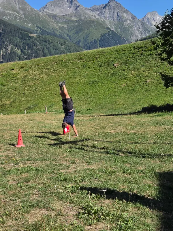 Das Bild zeigt einen Mann in einem schwarzen Hemd und schwarze Hosen, die auf einem üppigen grünen Hang stehen, mit einem roten Kegel vor… – Jugend und Hund Lager 2026 in Segnas
