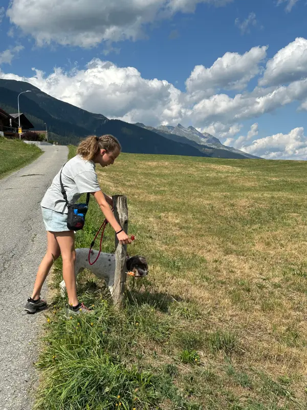 Eine Frau, die auf der Seite einer Strasse neben einem Gewässer steht und ein weisses T-Shirt und blaue Shorts trägt. Wandern. – Jugend und Hund Lager 2026 in Segnas