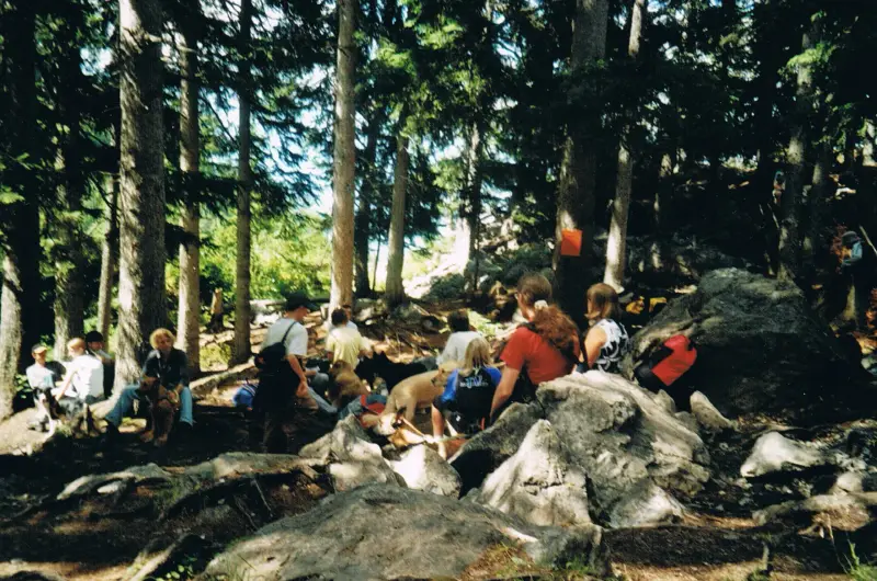 Eine Gruppe von Menschen, die auf Felsen im Wald sitzen. – Jugend und Hund Lager 2002 in Lenzerheide