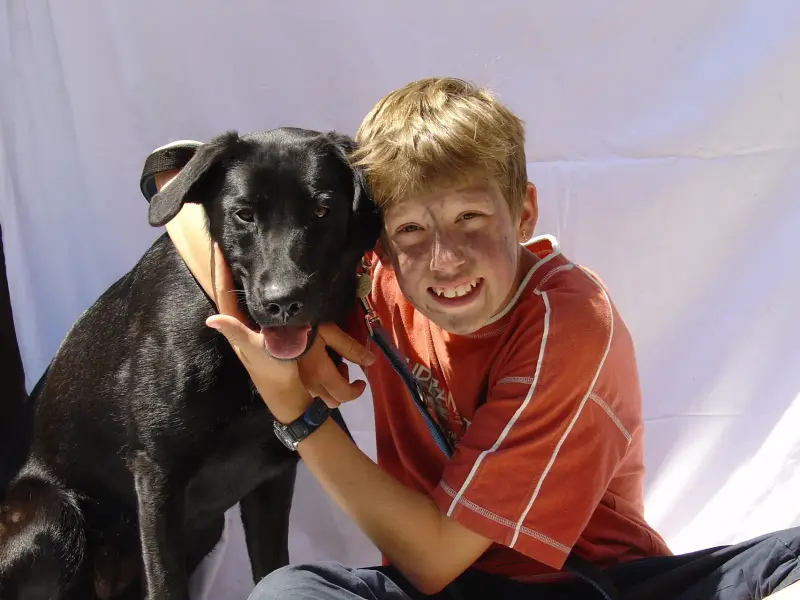 Ein Junge, der mit einem Hund auf dem Boden sitzt. – Jugend und Hund Lager 2003 in Lenzerheide