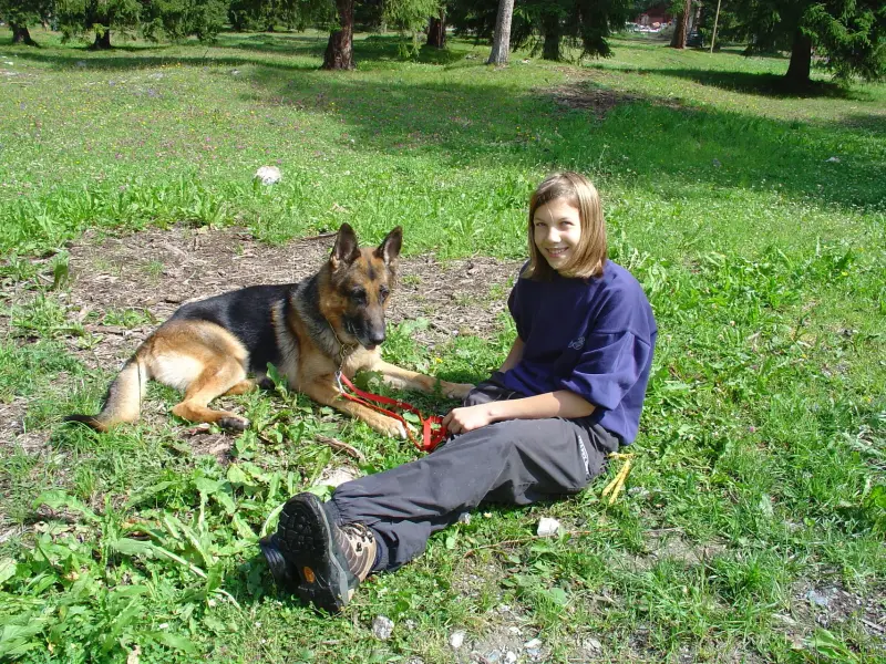 Ein junges Mädchen sitzt im Gras mit einem Hund. – Jugend und Hund Lager 2004 in Lenzerheide