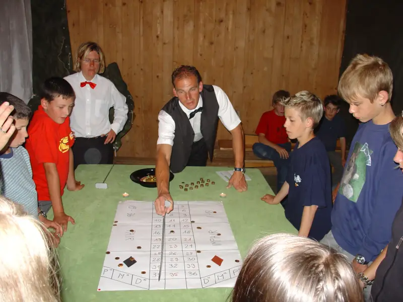 Eine Gruppe von Leuten, die um einen Tisch sitzen und ein Spiel spielen. – Jugend und Hund Lager 2004 in Lenzerheide