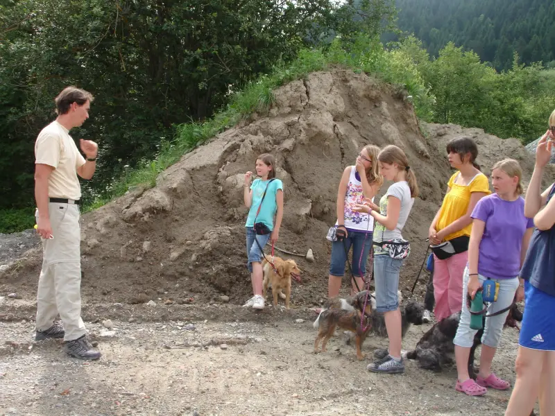 Eine Gruppe von Menschen, die um einen Haufen Dreck stehen, von denen einige Hunde halten. Rassen: Border Terrier, Golden Retriever. – Jugend und Hund Lager 2009 in Ruen