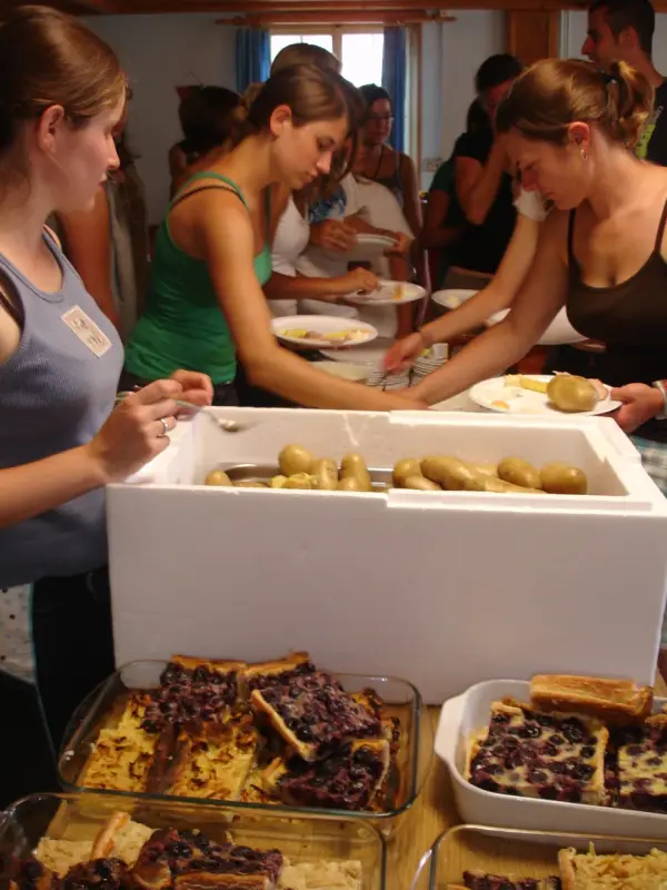 Eine Gruppe von Menschen, die um einen Tisch stehen, gefüllt mit Tabletts mit Lebensmitteln, Tellern und Löffeln. – Jugend und Hund Lager 2009 in Ruen