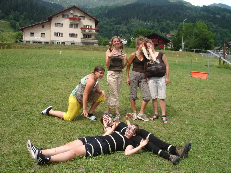 Eine Gruppe von Menschen, die auf einem üppigen grünen Feld liegen, umgeben von Gebäuden, Bäumen, Stangen, Lichtern und einem Zaun. – Jugend und Hund Lager 2009 in Ruen