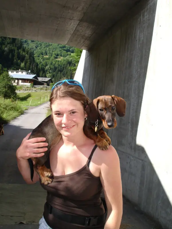 Eine Frau stehend und lächelnd, während sie einen kleinen braunen und schwarzen Dackel in den Armen hält. Rasse: Vizsla. – Jugend und Hund Lager 2009 in Ruen