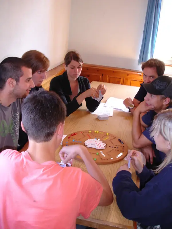 Eine Gruppe von Menschen, die um einen hölzernen Tisch sitzen und ein Spiel mit Brettspielen spielen. – Jugend und Hund Lager 2009 in Ruen