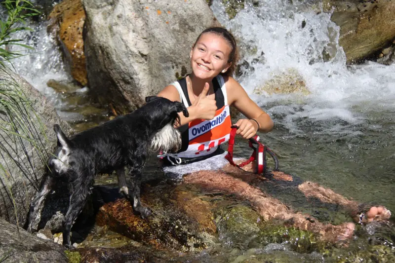 Eine Frau in einem nassen Anzug sitzt in einem Bach mit einem Hund. – Jugend und Hund Lager 2015 in Segnas