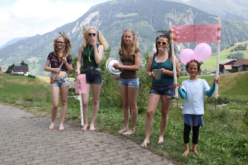 Eine Gruppe von fünf Frauen, die nebeneinander auf einer Strasse stehen und jeweils eine rosa Flagge halten. – Jugend und Hund Lager 2015 in Segnas