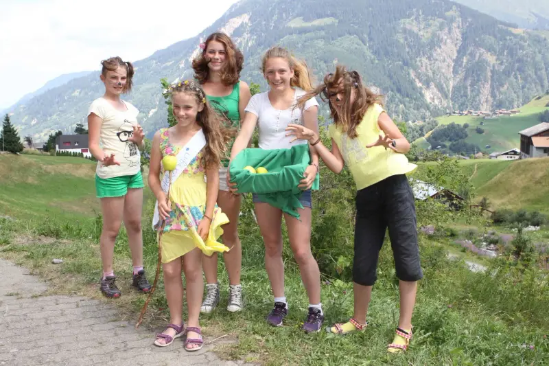 Eine Gruppe junger Frauen, die nebeneinander auf einer unbefestigten Strasse stehen, umgeben von üppig grünem Gras, Pflanzen, Bäumen und… – Jugend und Hund Lager 2015 in Segnas