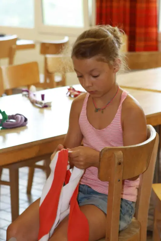 Ein kleines Mädchen sitzt an einem Tisch mit einer roten Krawatte. – Jugend und Hund Lager 2015 in Segnas