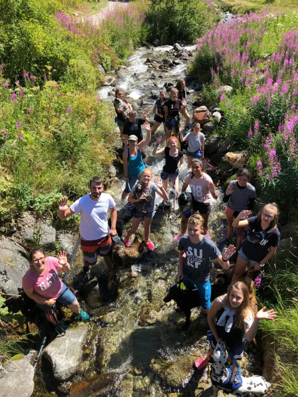 Eine Gruppe von Menschen, die auf Felsen in einem Bach sitzen. – Jugend und Hund Lager 2018 in Segnas
