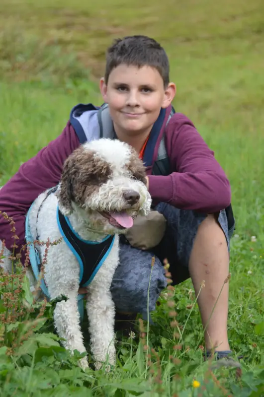 Ein Junge kniet auf einem Feld mit einem Hund. – Jugend und Hund Lager 2018 in Segnas