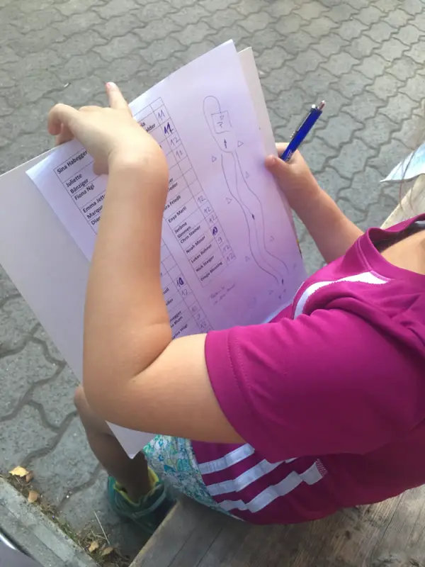Ein kleines Mädchen, das auf einer Bank sitzt und auf einem Stück Papier schreibt. – Jugend und Hund Lager 2018 in Segnas