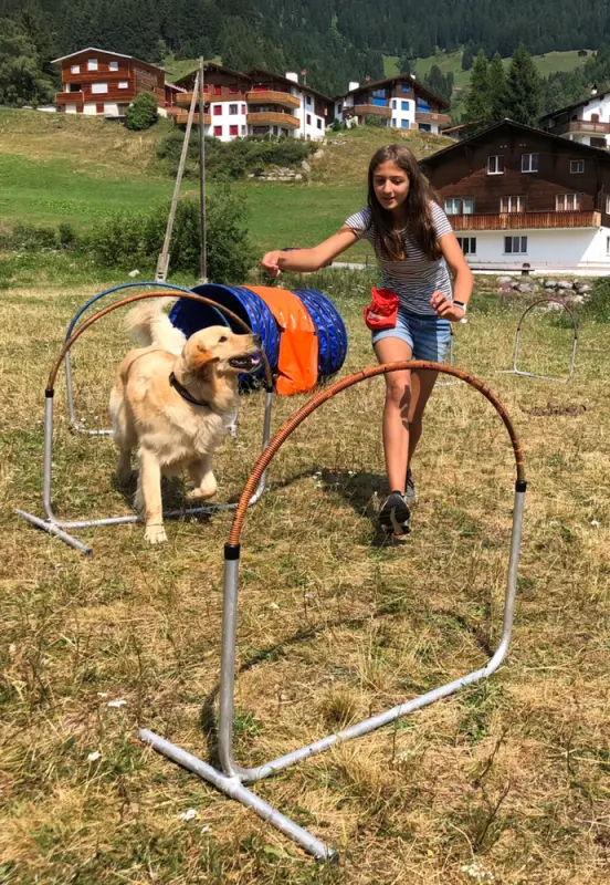 Ein junges Mädchen spielt mit einem Hund auf einem Feld. – Jugend und Hund Lager 2019 in Segnas