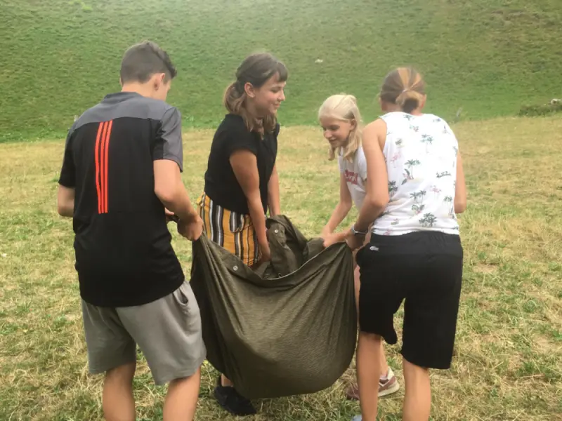 Eine Gruppe von Menschen, die um eine grosse Tasche stehen. – Jugend und Hund Lager 2019 in Segnas