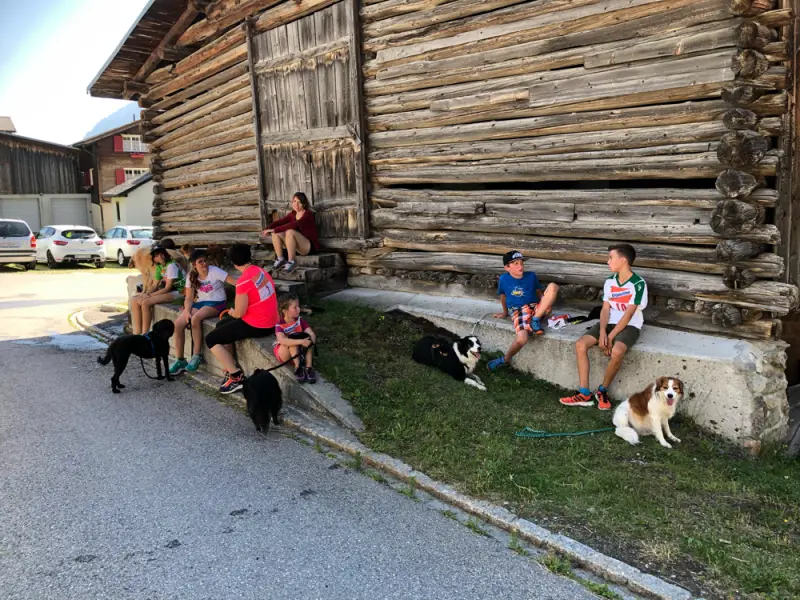 Eine Gruppe von Menschen, die auf der Seite eines Gebäudes sitzen. – Jugend und Hund Lager 2019 in Segnas