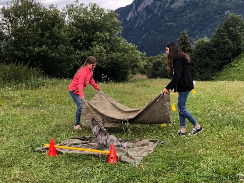 Zwei Mädchen spielen mit einer Plane im Gras. – Jugend und Hund Lager 2020 in Segnas