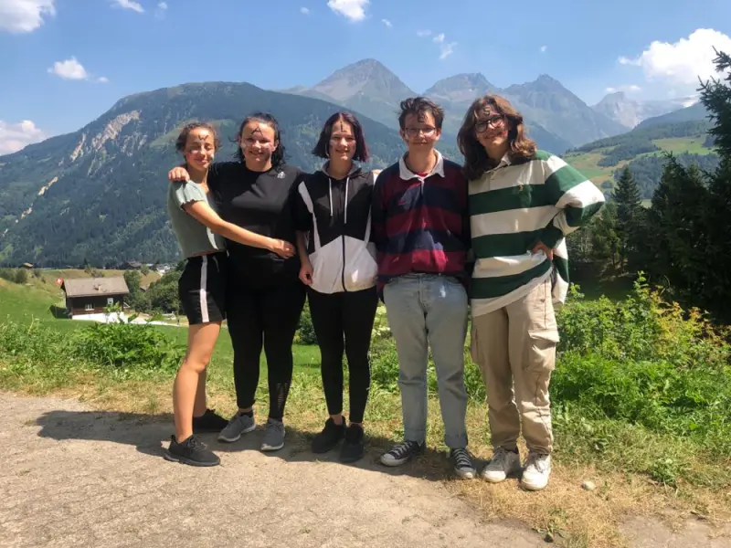 Drei Mädchen stehen auf einer unbefestigten Strasse vor den Bergen. – Jugend und Hund Lager 2022 in Segnas