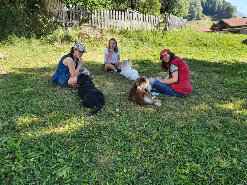 Drei Frauen sitzen im Gras mit ihren Hunden. – Jugend und Hund Lager 2022 in Segnas