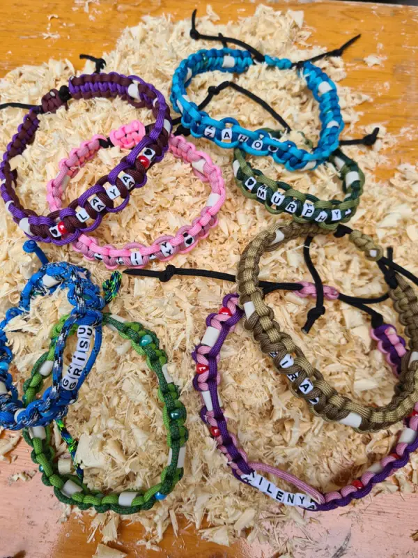 Das Bild zeigt einen Holztisch mit einer Reihe von bunten Paracord-Armbändern, die darauf sitzen. – Jugend und Hund Lager 2023 in Segnas