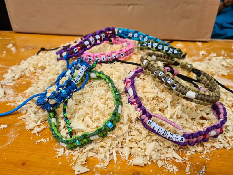 Das Bild zeigt einen Holztisch mit einer Reihe von bunten Paracord-Armbändern, die darauf sitzen. – Jugend und Hund Lager 2023 in Segnas