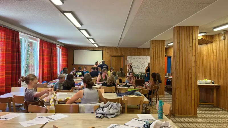 Eine Gruppe von Menschen, die an Tischen in einem Raum sitzen. – Jugend und Hund Lager 2024 in Segnas