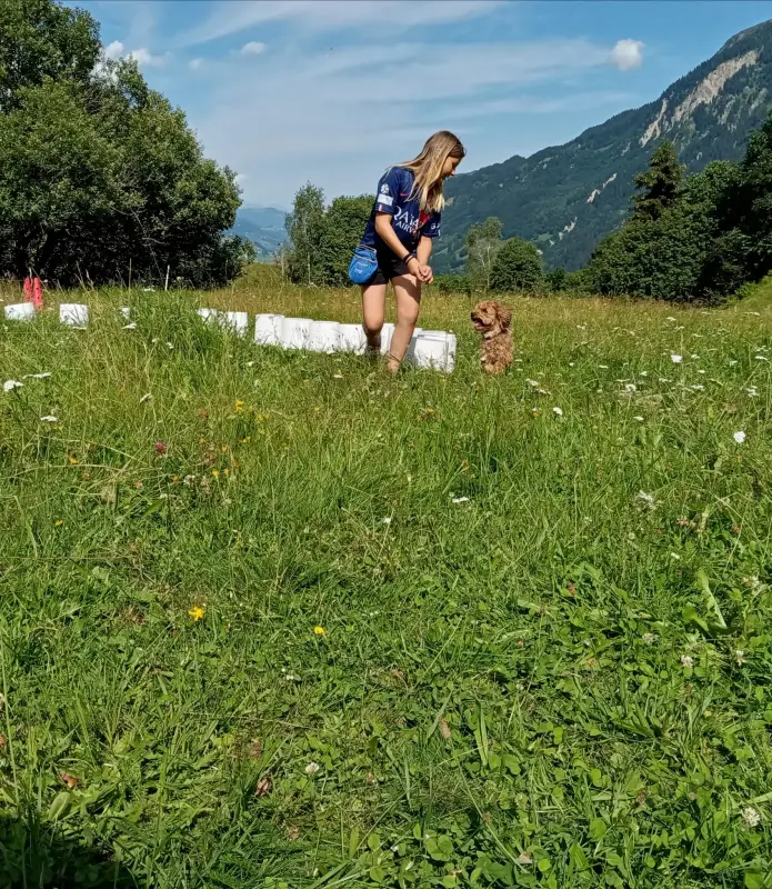 Eine Frau kniend unten auf einem Feld mit einem Hund. – Jugend und Hund Lager 2024 in Segnas