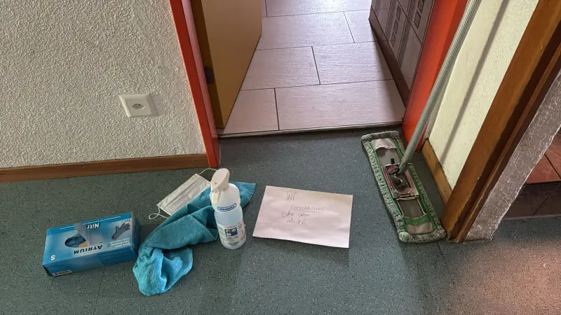 Das Bild zeigt einen Raum mit einem Mopp, einem blauen Handtuch, einer Flasche, einem Papier und einer Box auf dem Boden sowie eine Tür und… – Jugend und Hund Lager 2025 in Segnas