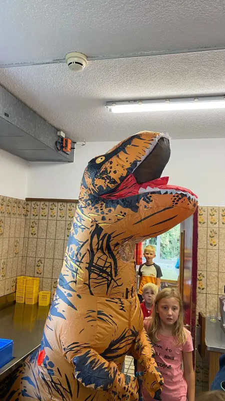 Eine Gruppe von Kindern, die um einen riesigen aufblasbaren Dinosaurier in einem Raum stehen. – Jugend und Hund Lager 2025 in Segnas