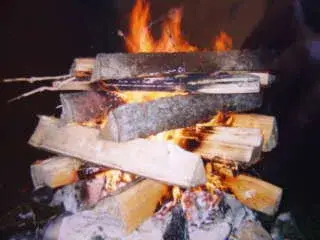 Das Bild zeigt einen Brennholzhaufen, der auf einem Tisch sitzt, wobei die Flammen um die Holzstücke herum lecken. – Jugend und Hund Lager 2000 in Sörenberg