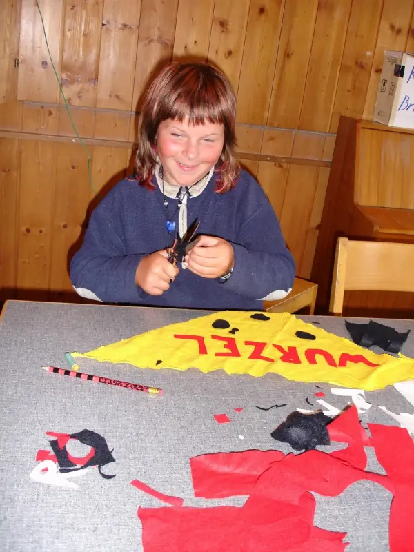 Ein junges Mädchen sitzt an einem Tisch mit einem Stück Papier. – Jugend und Hund Lager 2006 in Trans