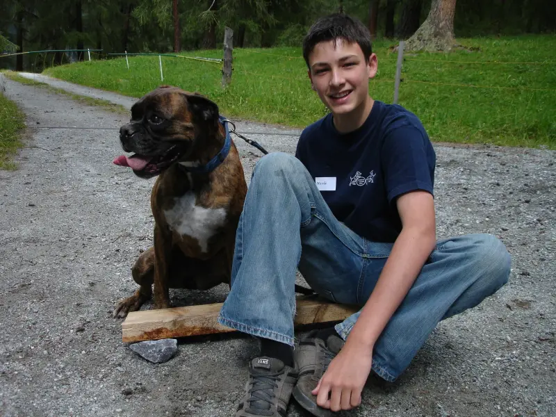 Ein Junge sitzt auf einer Holzbank mit einem Hund. – Jugend und Hund Lager 2007 in Trans